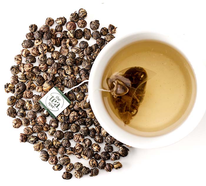 
                  
                    jasmine pearls loose leaf tea sit next to a cup of steeped tea with a green tea bag in it
                  
                