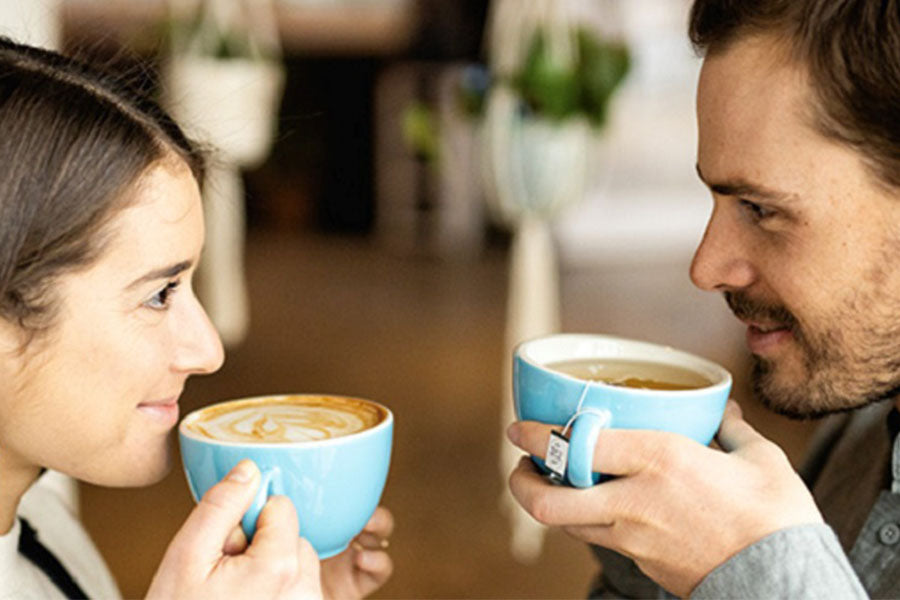 a woman holds a coffee cup and is looking at a man holding a tea cup