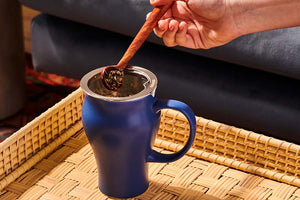 a hand is holding a spoon putting loose leaf tea into a tea mug