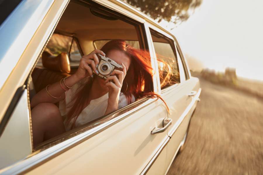 a woman leans out of a car window snapping a picture on a camera