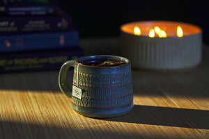 a tea mug with a tea bag sits in front of a candle