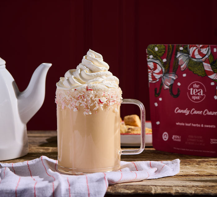 Candy Cane Craze tea with whipped cream and candy cane pieces next to a 'Candy Cane Craze' tea package on a wooden surface.
