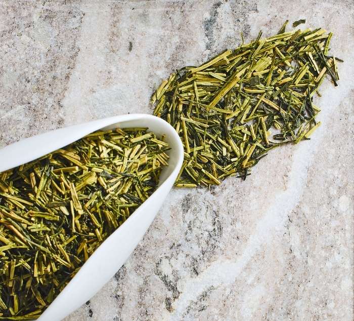 Kukicha green tea leaves in a white scoop on a marble surface