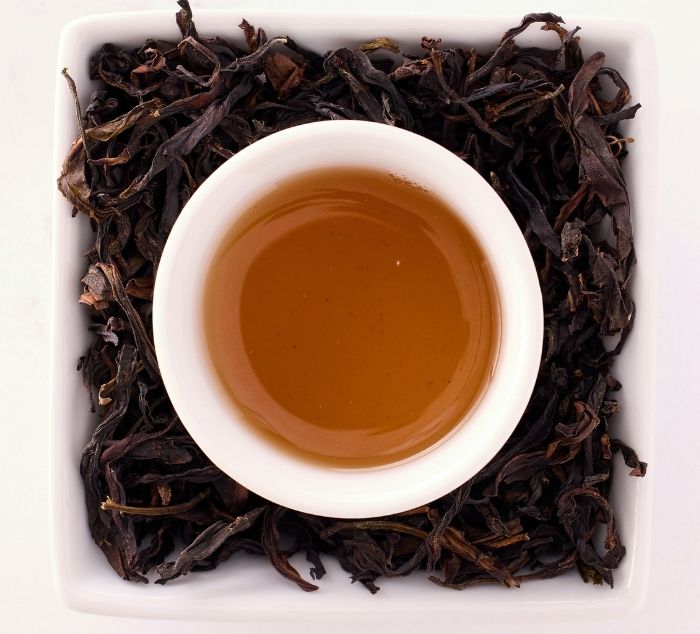 White cup of mi lan xiang tea surrounded by dry tea leaves on a white background