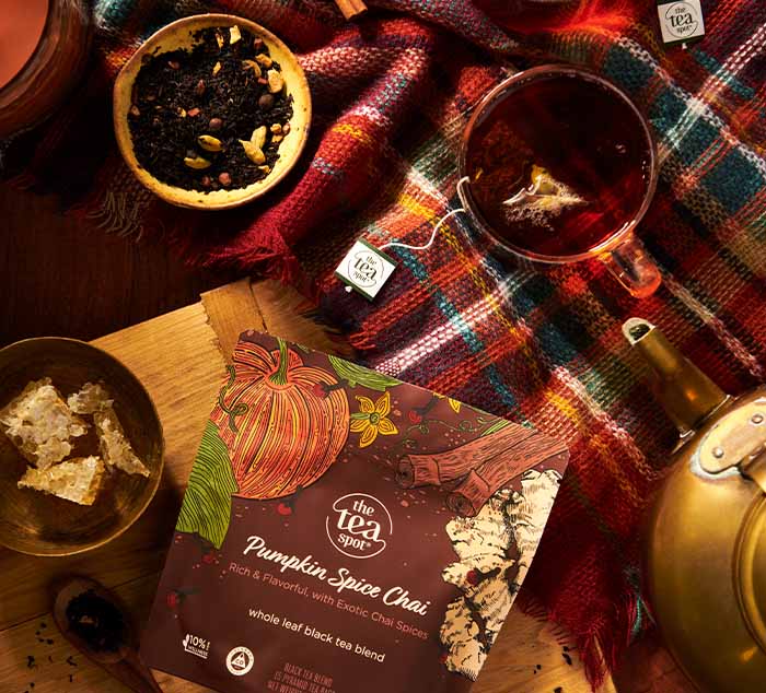 Tea packaging with pumpkin spice chai, tea leaves, and a teacup on a colorful plaid cloth.