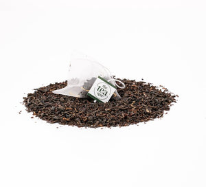 a tea bag filled with black tea sits on top of a pile of loose leaf black tea