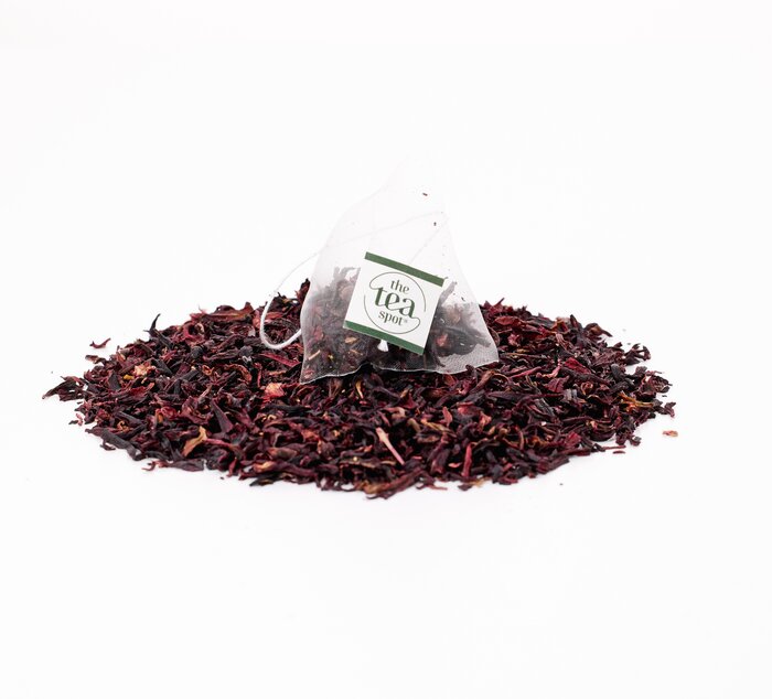 
                  
                    a tea bag filled with hibiscus tea sits on top of a pile of loose leaf hibiscus tea
                  
                