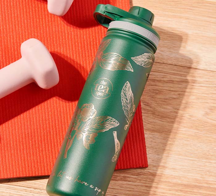 a green tea tumbler lies on the floor on a yoga mat with weights alongside