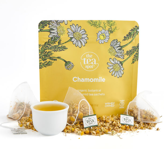 Yellow packaging of organic chamomile tea with a cup of tea and loose chamomile flowers on a white background