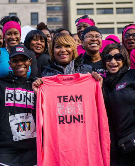women smile holding a pink shirt that says team black girls run!