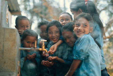 many children smile as they wash their hands at a water spigot