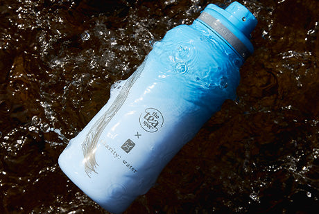 a water bottle reading the tea spot and charity:water rests in a creek
