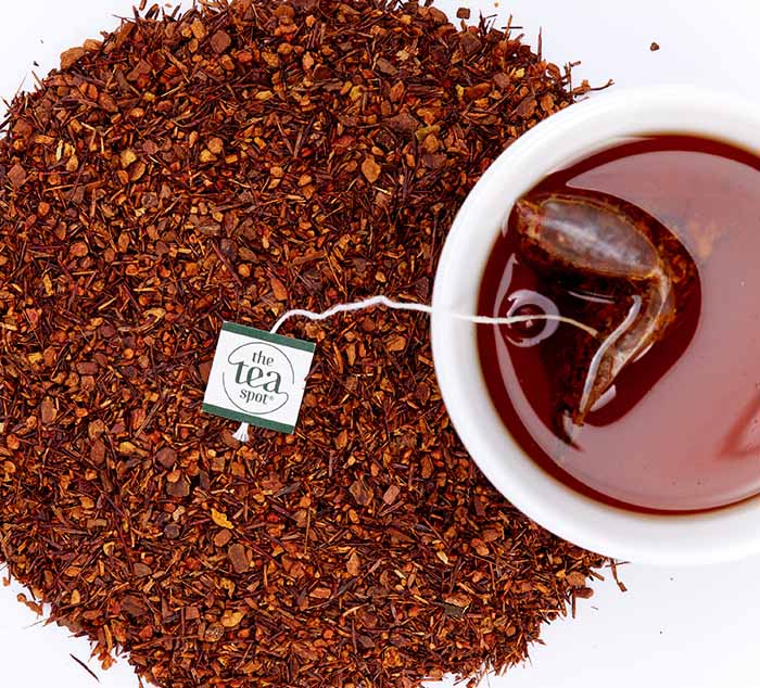 a cup of brewed tea with a tea bag in it surrounded by loose leaf tea