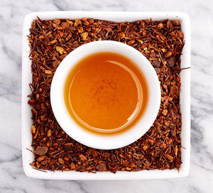 a cup of brewed cinnamon spice tea sits in a dish with loose leaf cinnamon tea in it