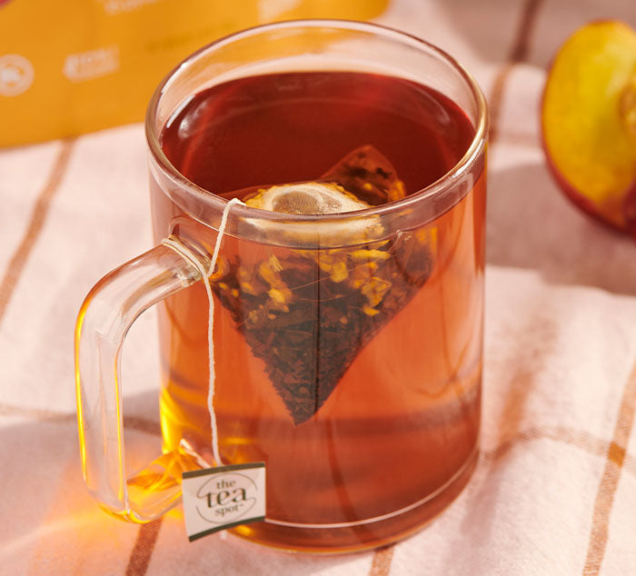 
                  
                    Glass mug with black tea and a tea bag on a checkered tablecloth.
                  
                