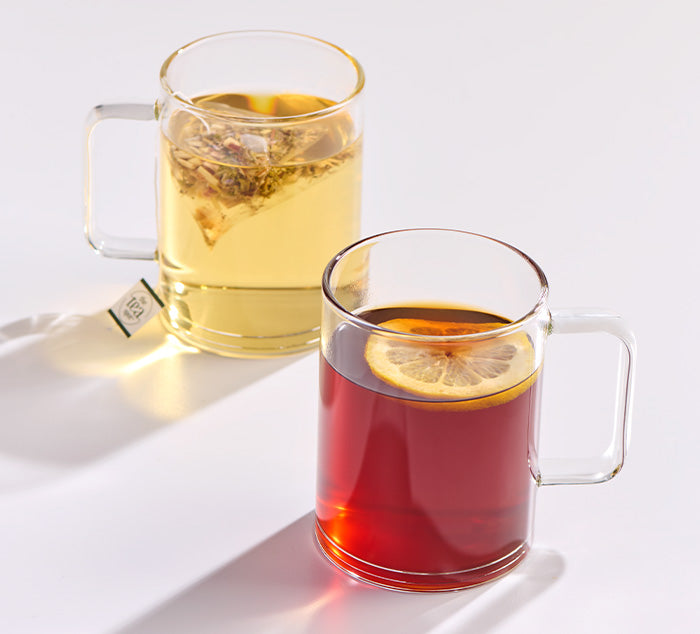 two clear tea mugs with tea brewing in them on a white surface