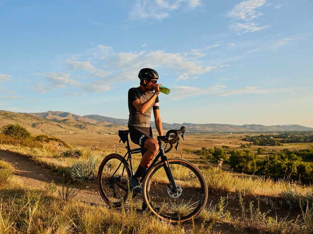cyclist on mountain breaks and sips tea out of tea brewing bottle