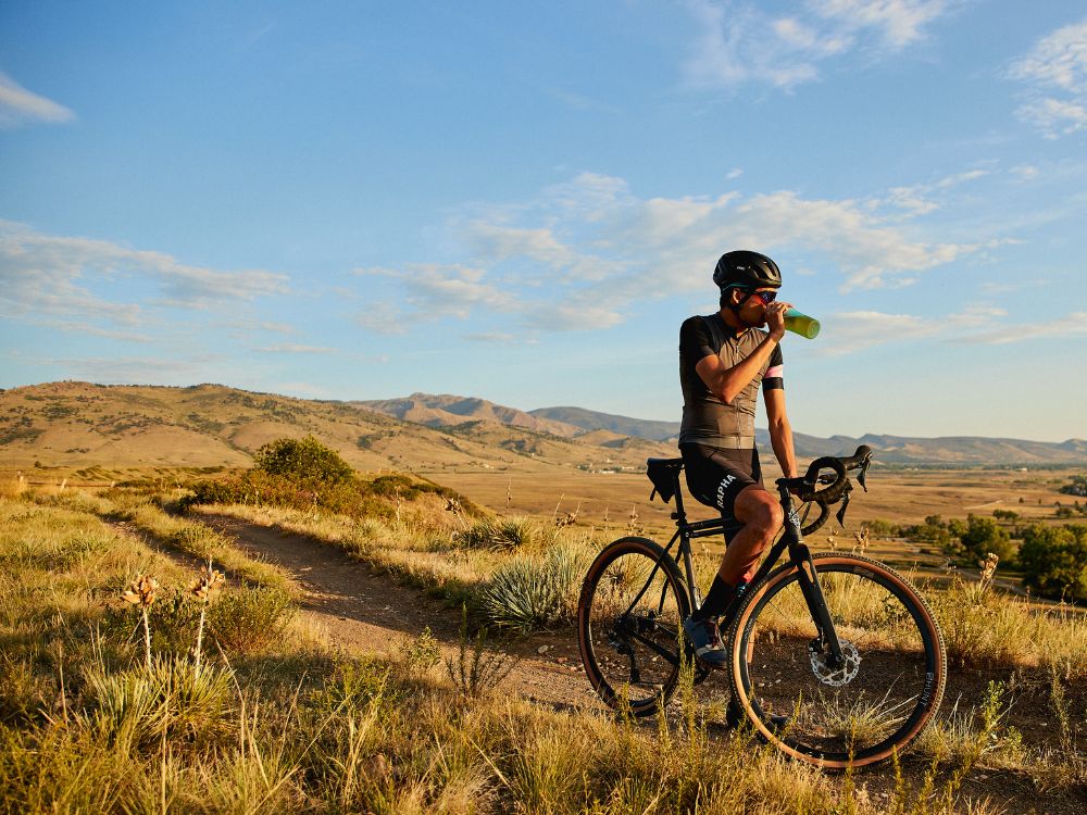 cyclist on mountain breaks and sips tea out of tea brewing bottle