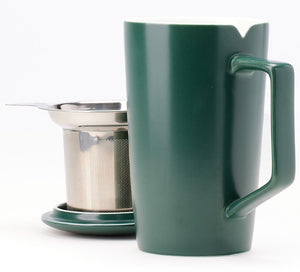 a green ceramic tea mug sits in the foreground with a stainless steel tea infuser and lid behind it