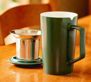 a green tea mug sits on a table with a tea infuser and tea mug lid next to it