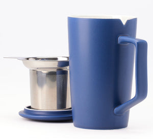 a blue ceramic tea mug sits in the foreground with a stainless steel tea infuser and lid behind it