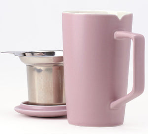 a pink ceramic tea mug sits in the foreground with a stainless steel tea infuser and lid behind it