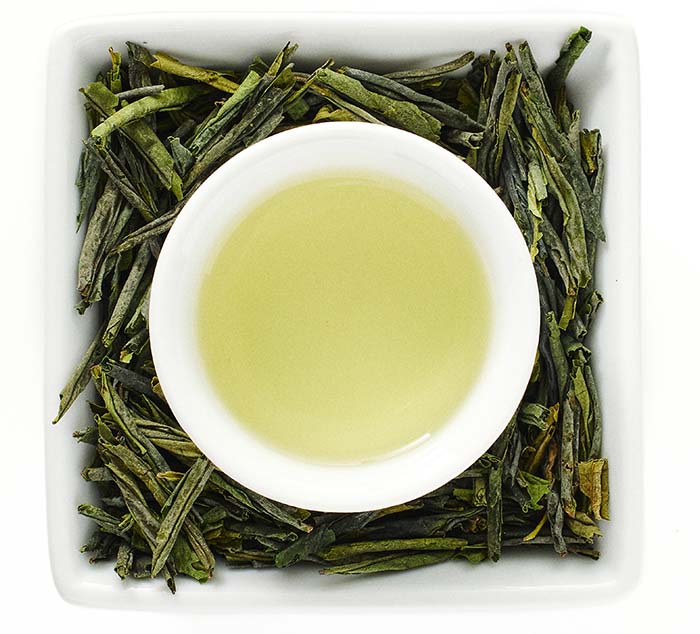 White bowl with lu'an guapian green tea surrounded by green tea leaves on a white background
