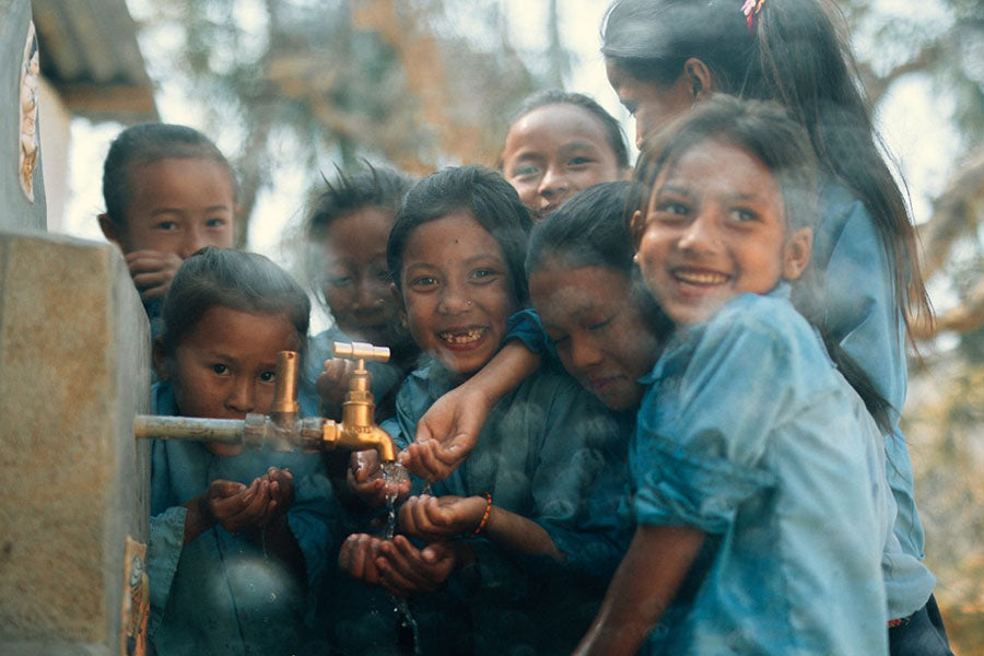children crowd around a water spigot washing their hands with clean water
