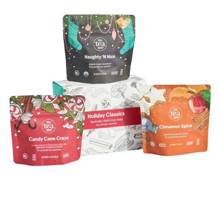 Three stand-up pouches of The Tea Room tea products arranged on a white background: a black 'Naughty Nice' pouch at the top, a red 'Candy Cane Craze' pouch at lower left, and an orange 'Cinnamon Spice' pouch at lower right, with a white box reading holiday classics between them.
