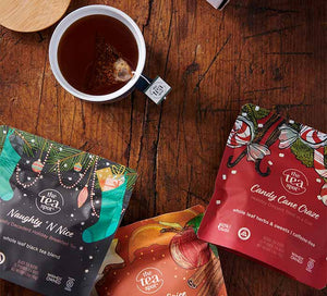 three pouches of holiday tea sit on a table with a mug of brewed tea