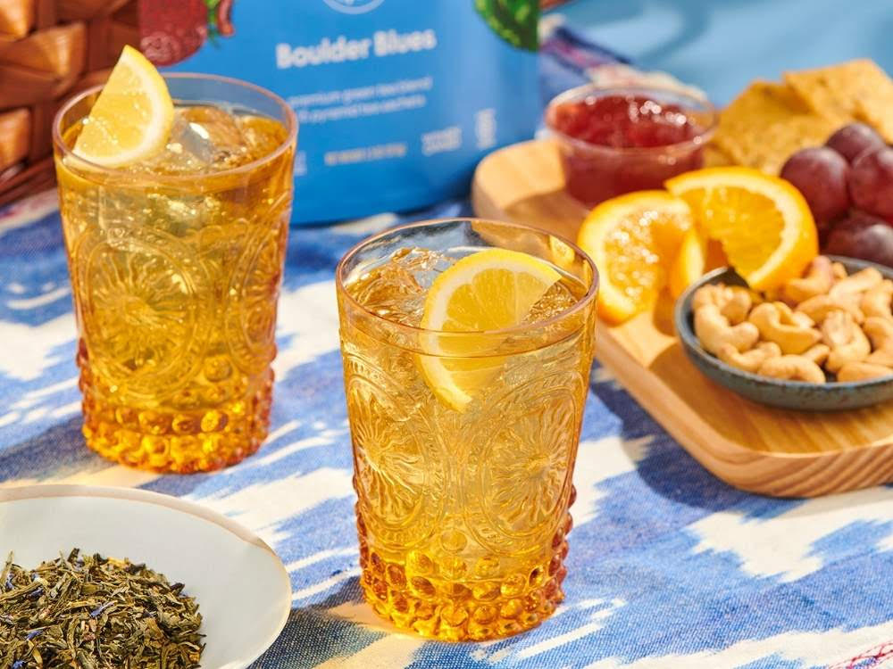 two glasses of iced tea sit on picnic table with food and bag that says Boulder Blues