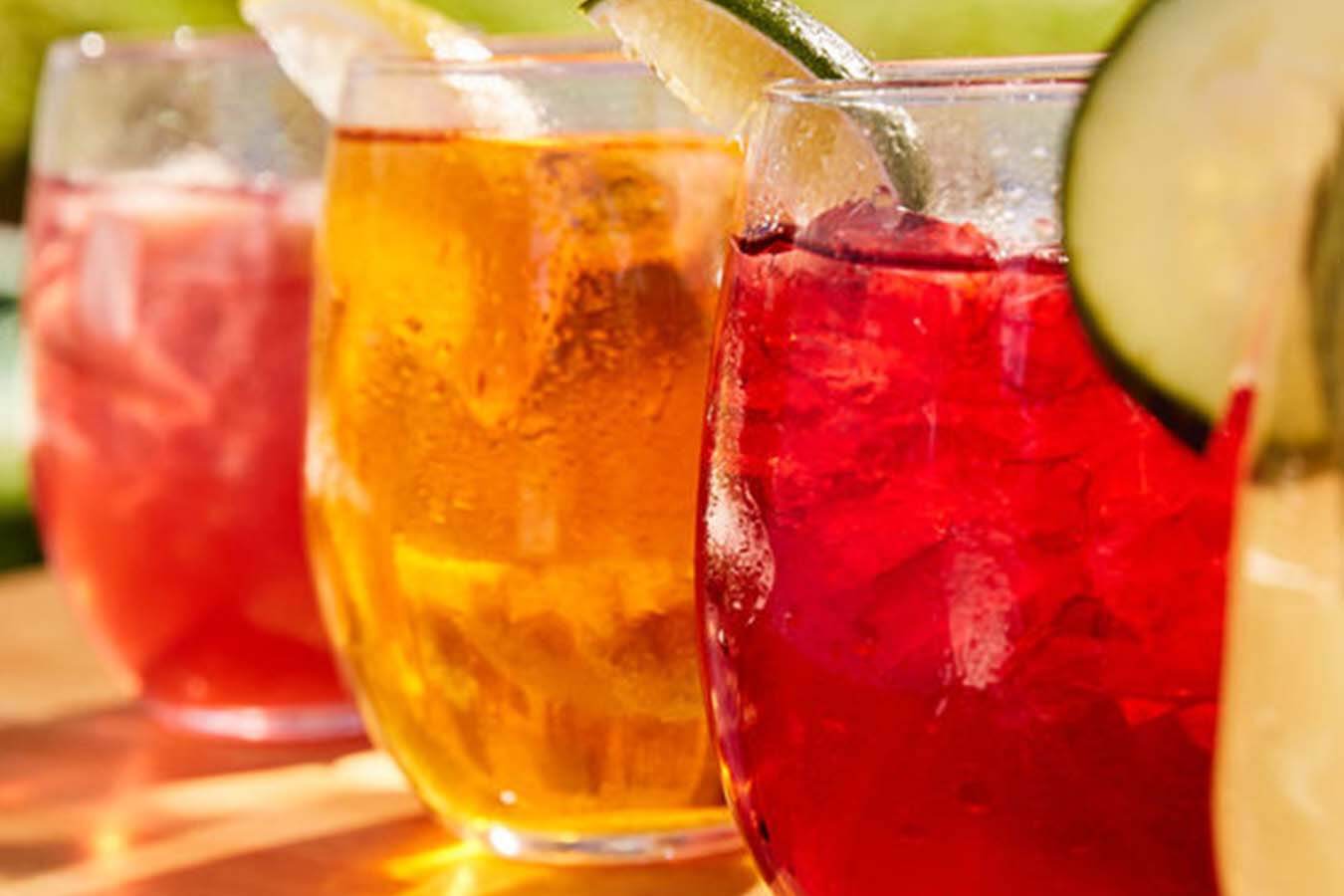 four glasses of iced tea with fruits sit on a wooden table