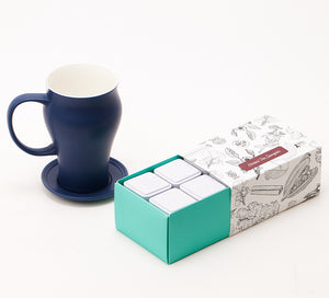an herbal tea sampler with loose leaf tea tins sits in front of a blue mug sitting on a saucer