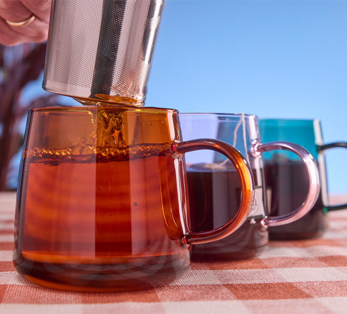 
                  
                    Tea being steeped into a colored tea mug on a checkered tablecloth.
                  
                