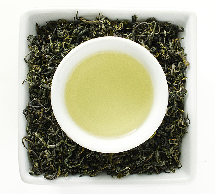 White cup with pan long yin hao green tea leaves and brewed tea on a white background