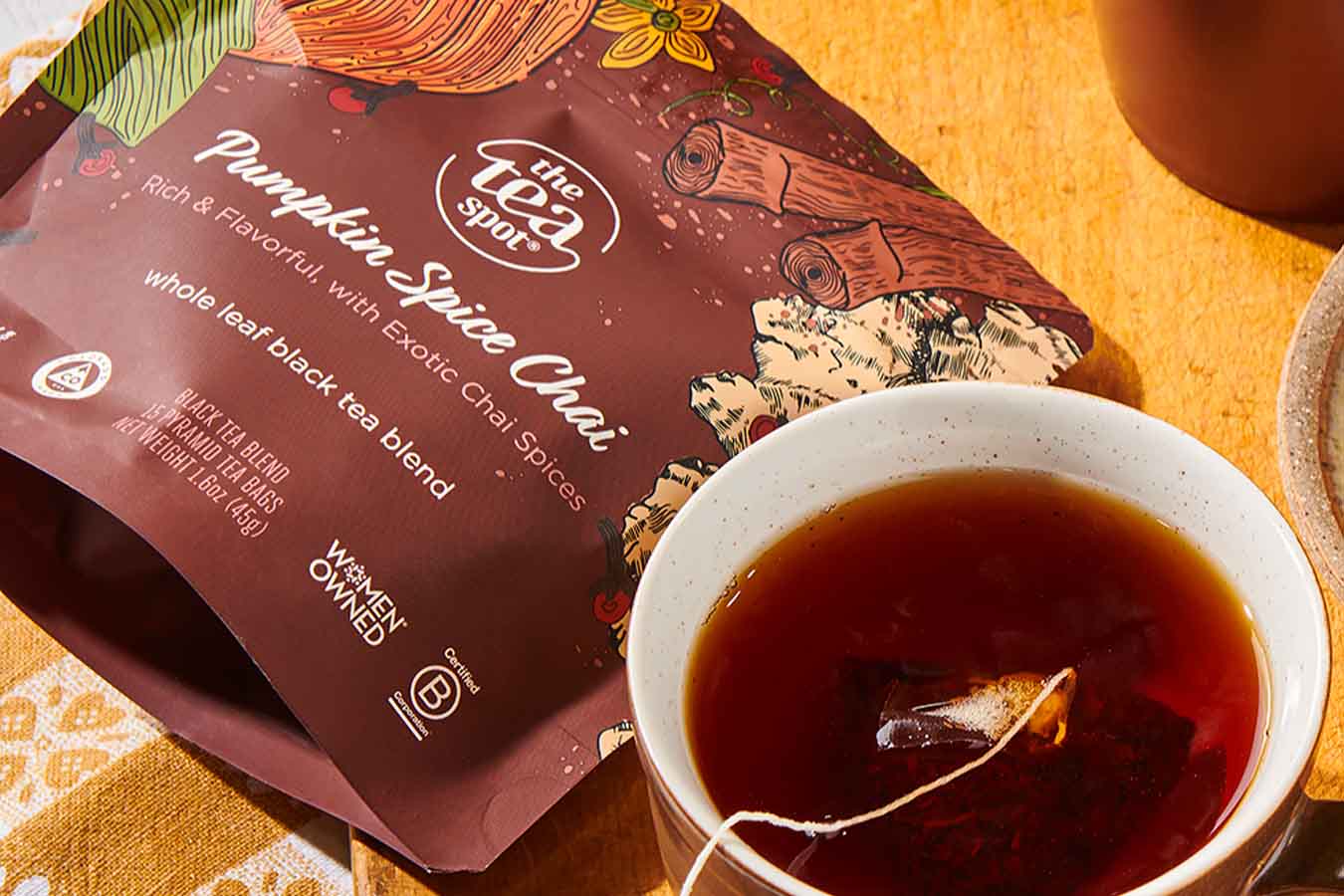 a bag of tea reading pumpkin spice chai sits next to a mug with a tea bag steeping in it