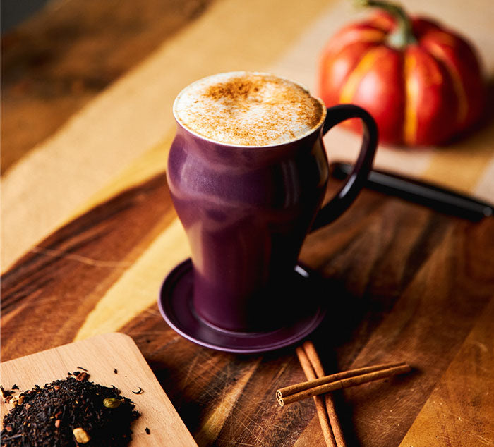 
                  
                    a pumpkin spice chai latte is in a purple mug sitting on a table with a pumpkin and pumpkin spices
                  
                