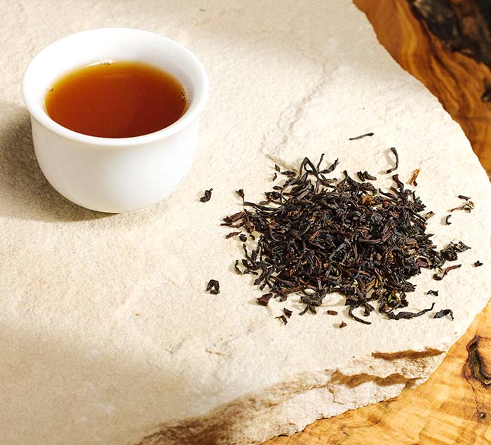 a pile of puttabong darjeeling tea leaves sits next to a brewed cup of tea