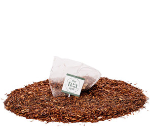 a tea bag filled with herbal rooibos tea sits on top of a pile of loose leaf herbal tea