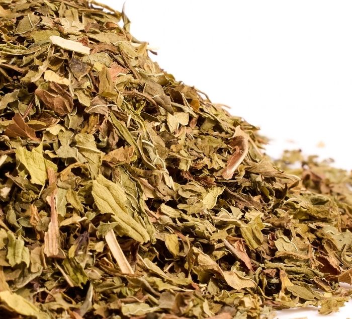A pile of loose leaf spearmint tea leaves, photographed close-up against a white background.