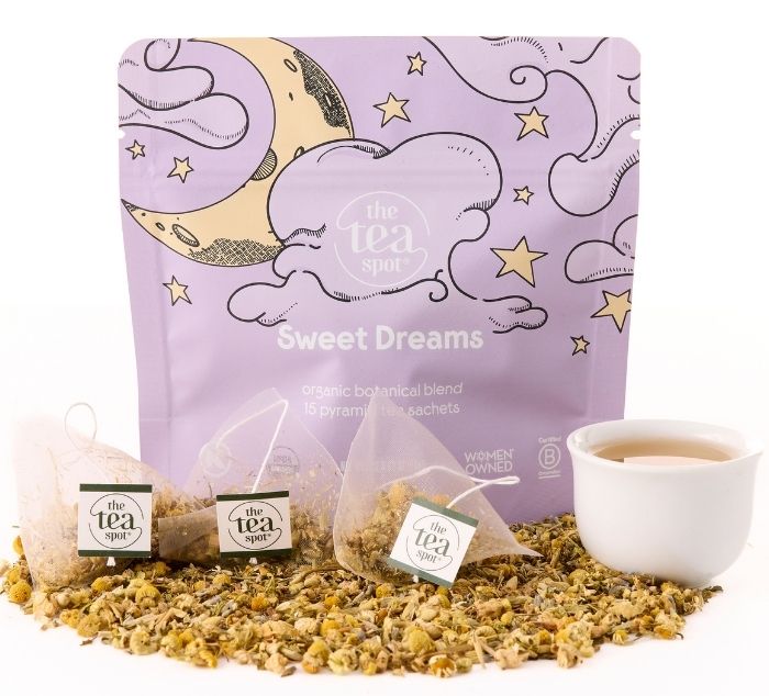 lavender pouch labeled sweet dreams sits on loose leaf tea next to tea sachets and a brewed cup of tea