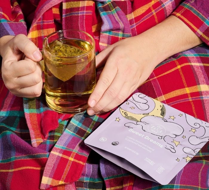 a person holds a cup of sweet dreams sleepy tea on their lap in a robe