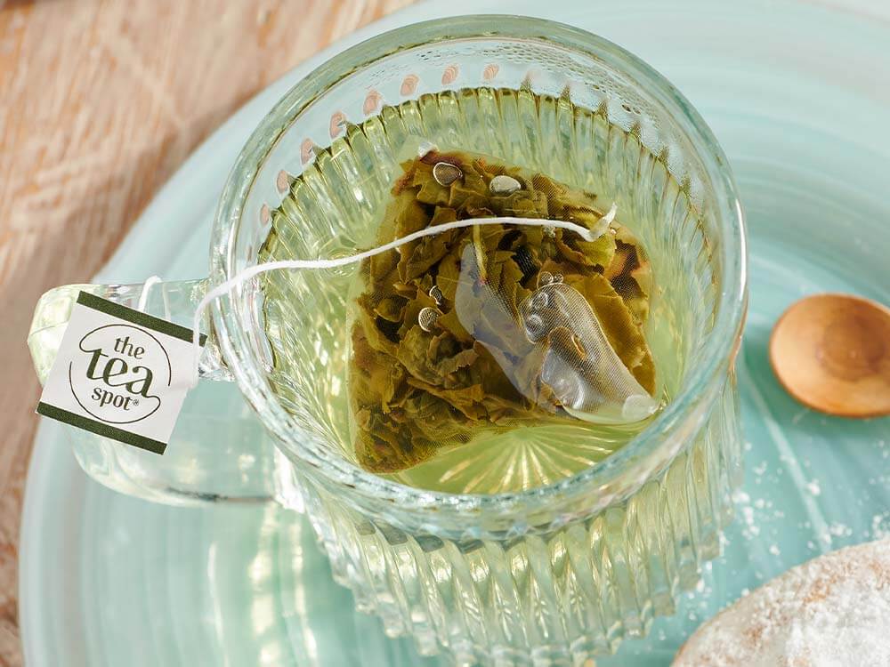 a plastic free tea bag steeps in a glass cup of tea