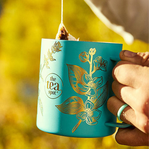 a person takes a tea bag out of a teal tea cup