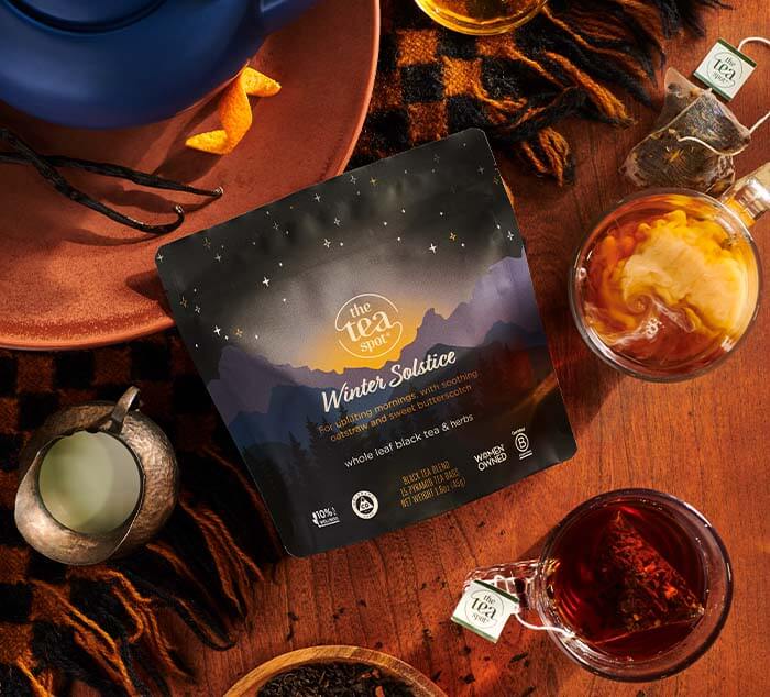 Winter Solstice Tea pouch displayed on a cozy winter setup with warm tones, featuring a teapot, a steaming cup of tea, and festive seasonal details like a blanket and milk pitcher.