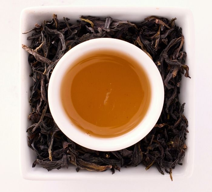 White cup of ya shi xiang tea surrounded by dry tea leaves on a white background