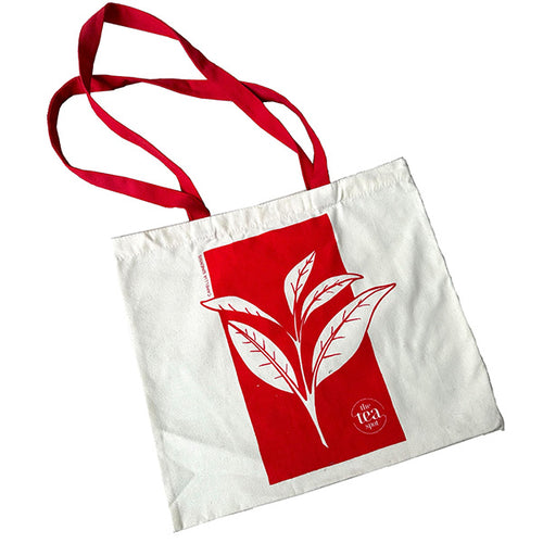 a white tote bag with a tea leaf design in red