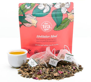 meditative mind tea bags sitting on a pile of loose leaf tea in front of a pink bag reading meditative mind "whole leaf white tea blend with herbs"