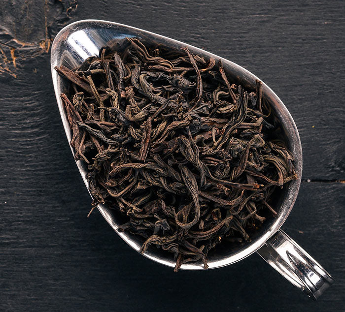 
                  
                    Yunnan black tea leaves in a silver dish placed on a black wooden table
                  
                
