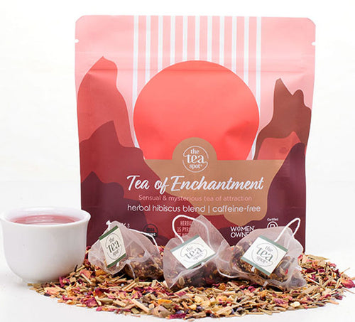 three tea bags sit on a pile of loose leaf herbal tea in front of a bag that reads tea of enchantment